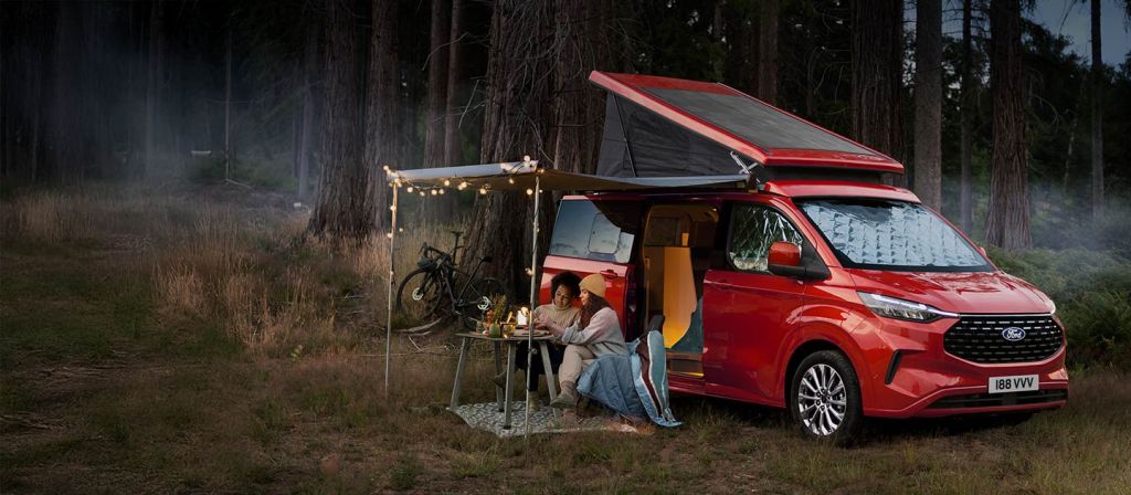 Ford Transit Custom Nugget roja con el techo elevable abierto y el toldo desplegado en un bosque