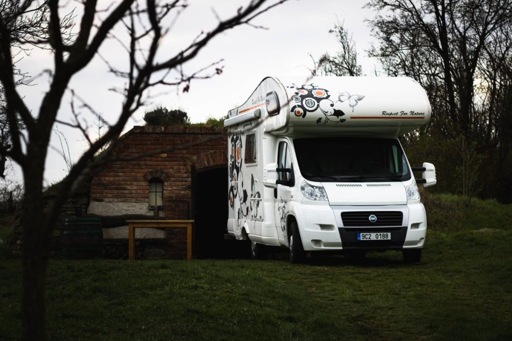 Autocaravana capuchina blanca aparcada junto a un cobertizo