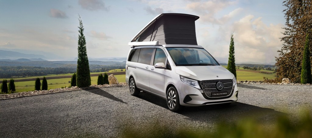 Mercedes-Benz Marco Polo blanca con el techo elevable abierto en un camino de grava entre cipreses