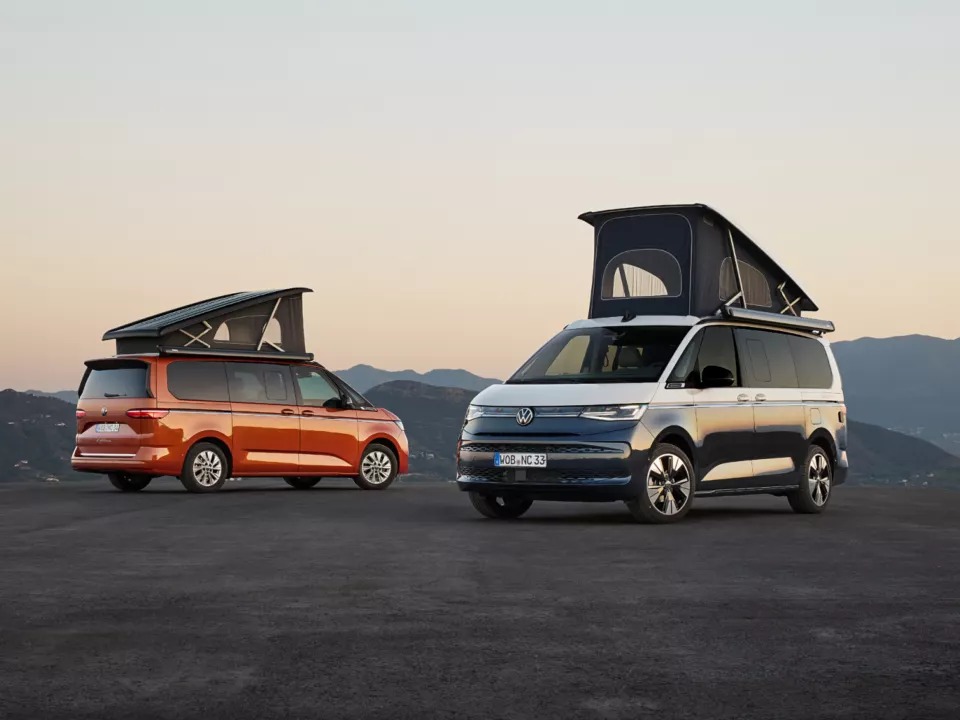 Volkswagen California naranja con el techo elevable abierto frente a unas montañas al atardecer